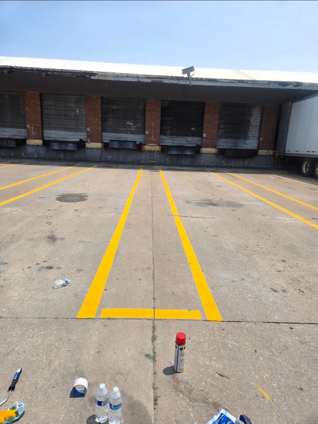 A loading dock with freshly painted yellow parking stripes, cans of spray paint, and supplies on the concrete ground.