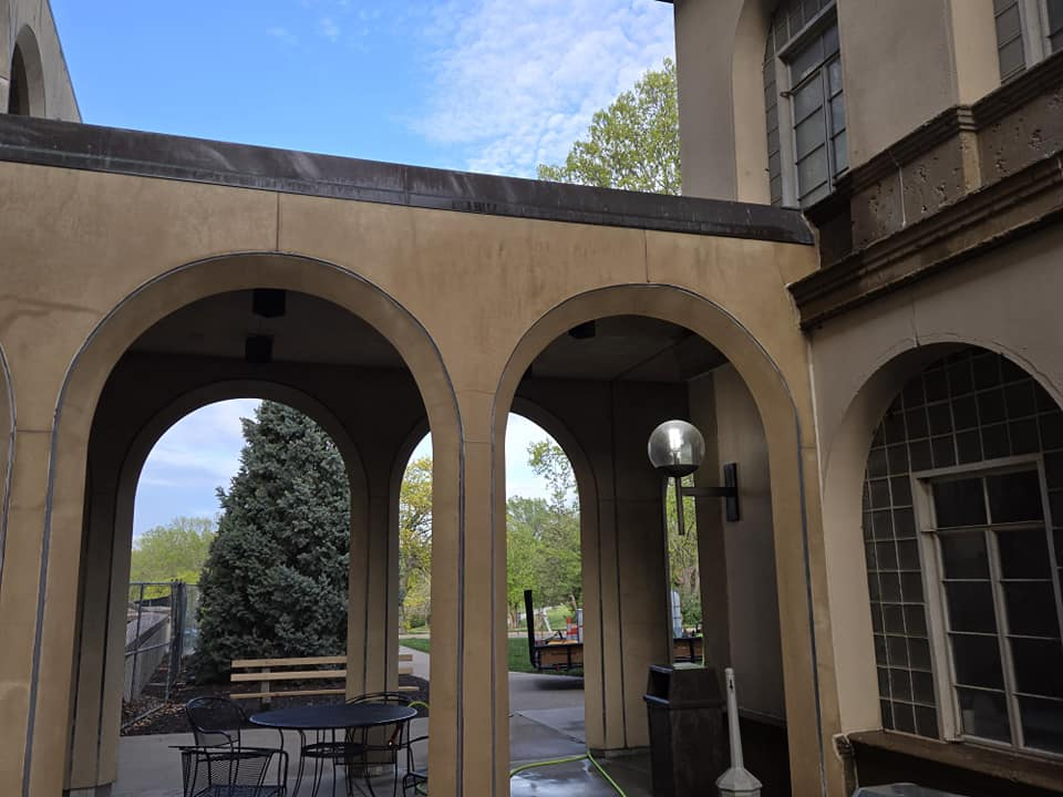 A tan covered patio with two stone archways leading to a garden view, with patio furniture in the foreground.