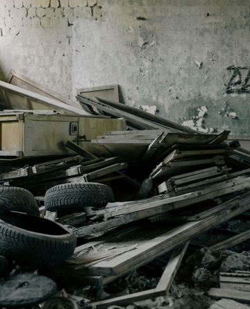 A pile of debris, including discarded tires and wooden boards, sits inside a derelict building with weathered walls.