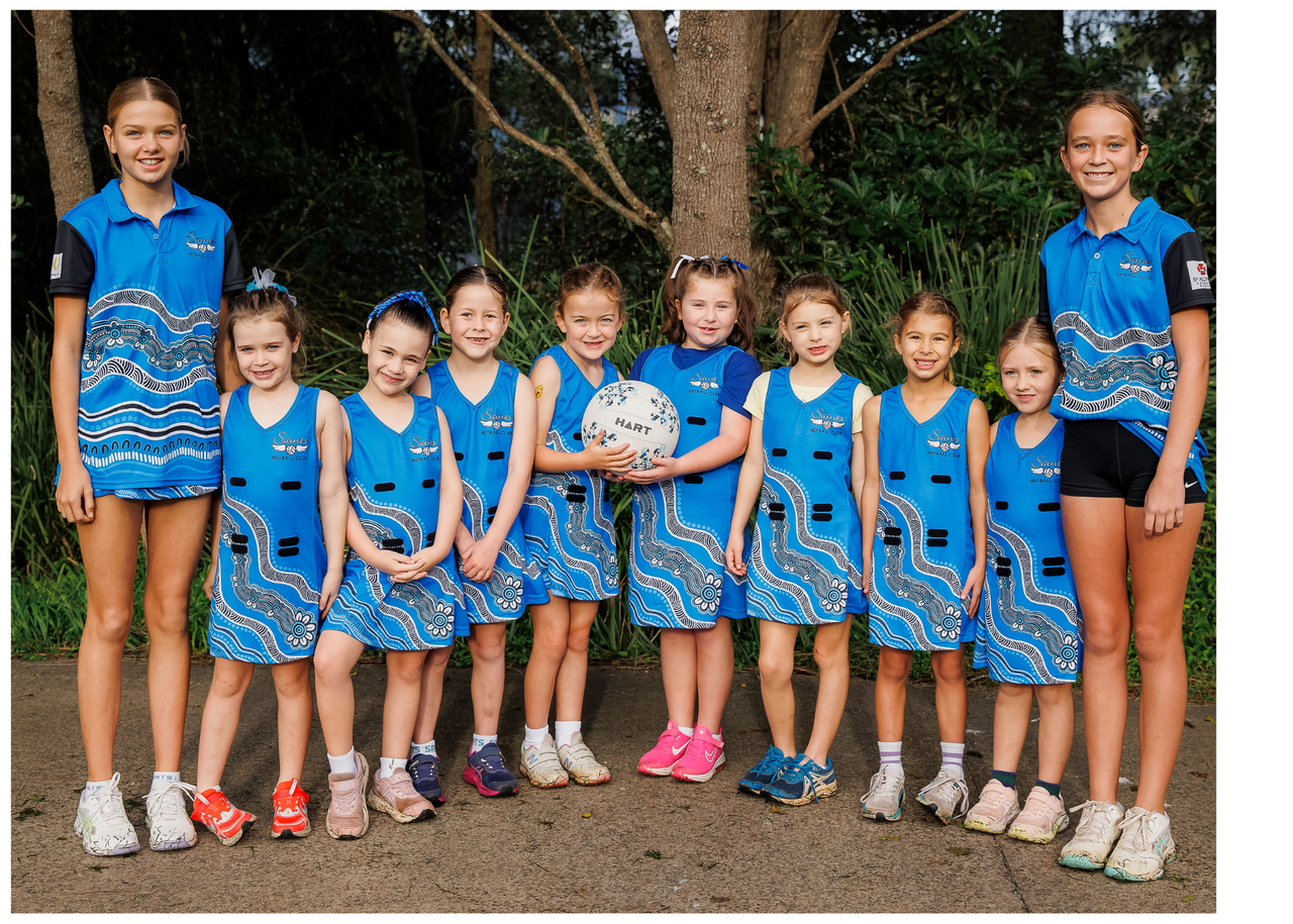 Cheer team group photo outdoors in matching blue uniforms, standing in front of trees