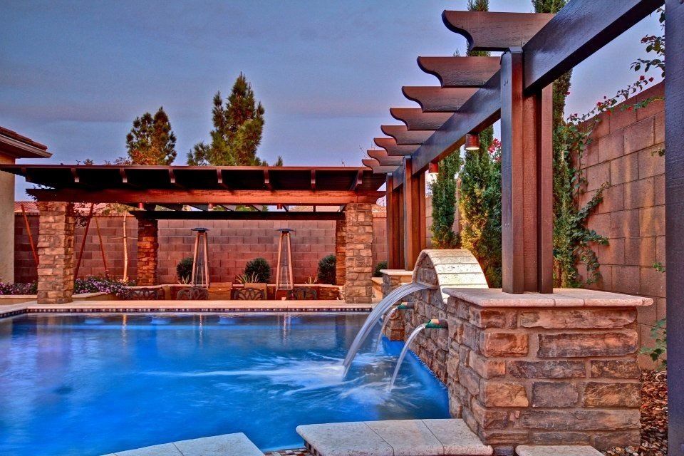 A large swimming pool with a waterfall and a pergola