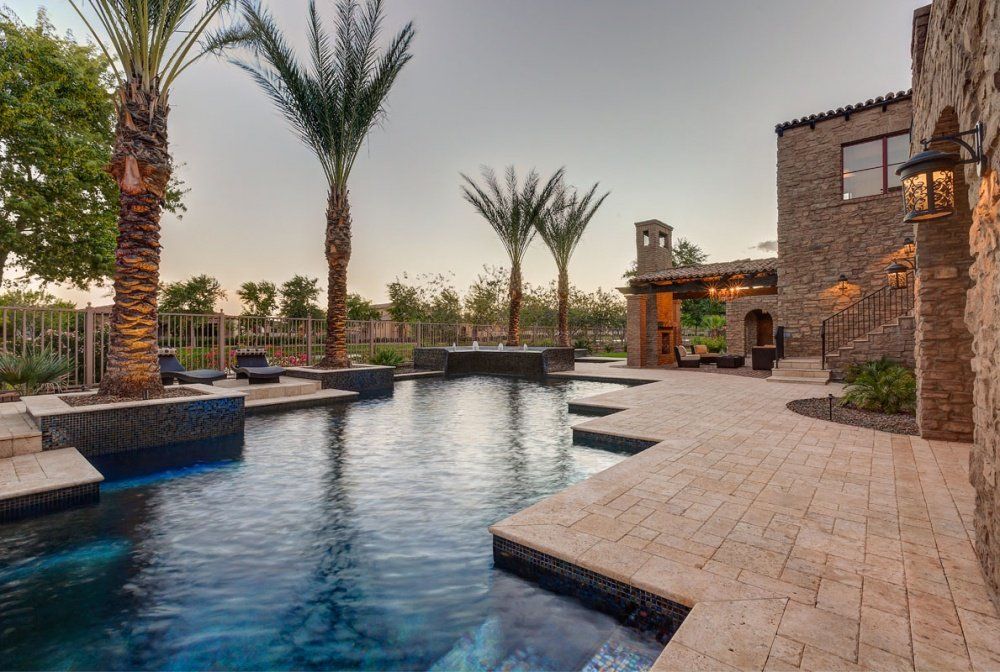 A large swimming pool surrounded by palm trees in front of a large stone building.