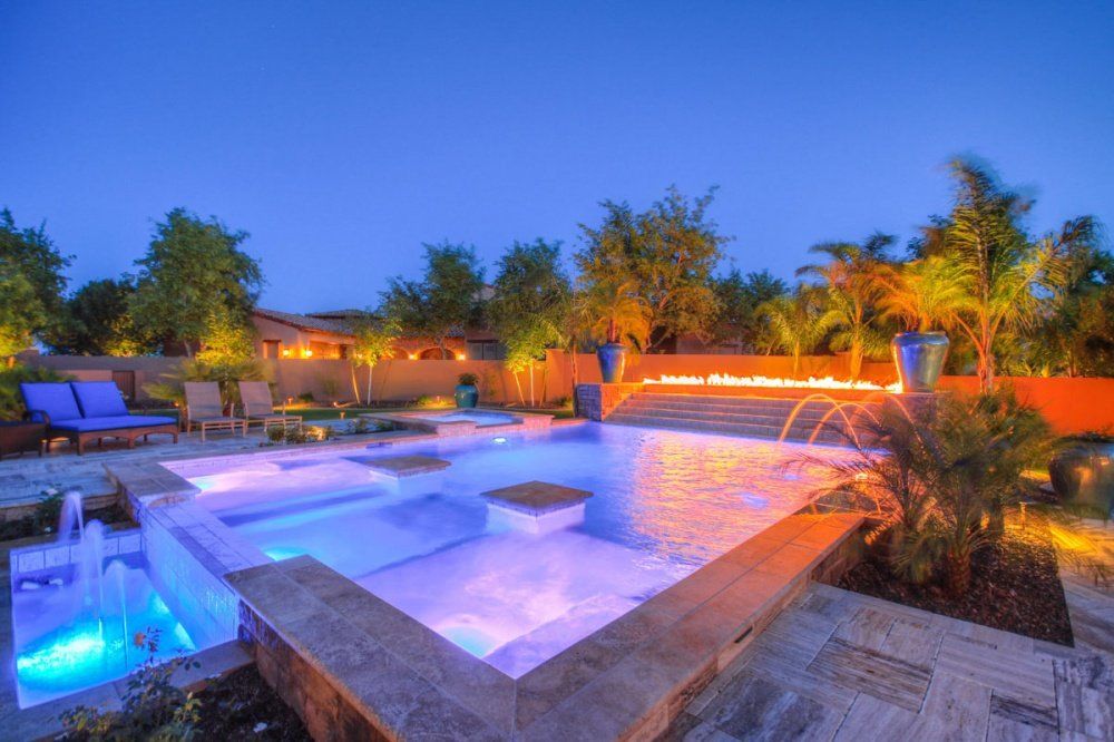 A large swimming pool is lit up at night in a backyard.