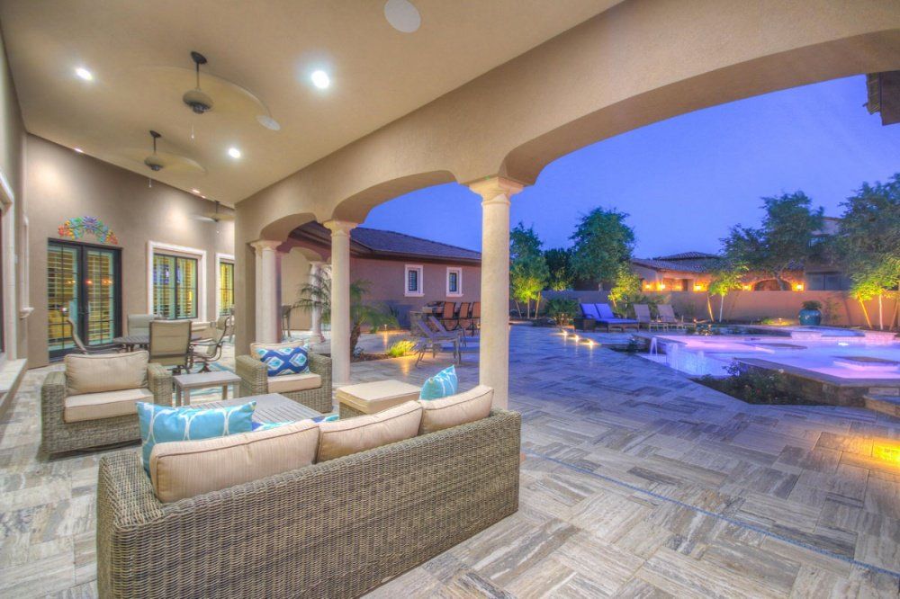 A patio with a couch , chairs , and a table with a pool in the background.