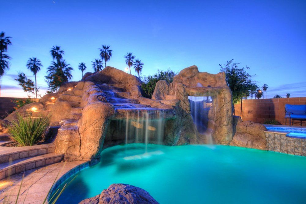 A swimming pool with a waterfall and palm trees in the background