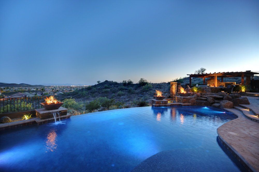 A large swimming pool is lit up at night with a view of a city.