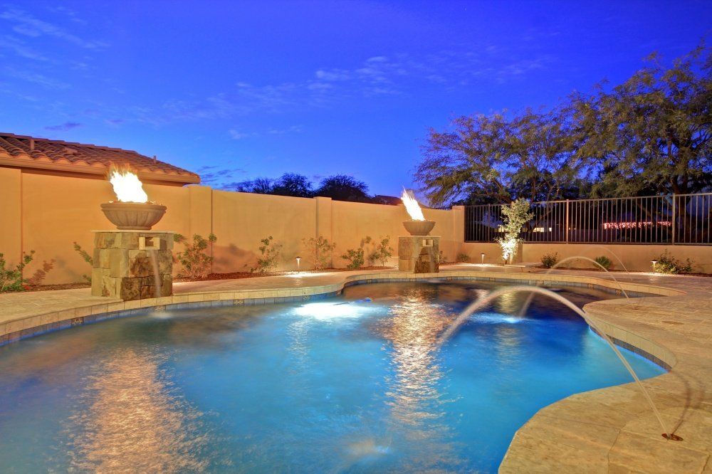 A large swimming pool with a fountain in the middle of it at night.