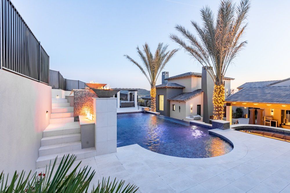 A large swimming pool is surrounded by palm trees and a house.