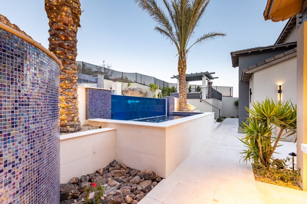 A swimming pool in the backyard of a house with palm trees.