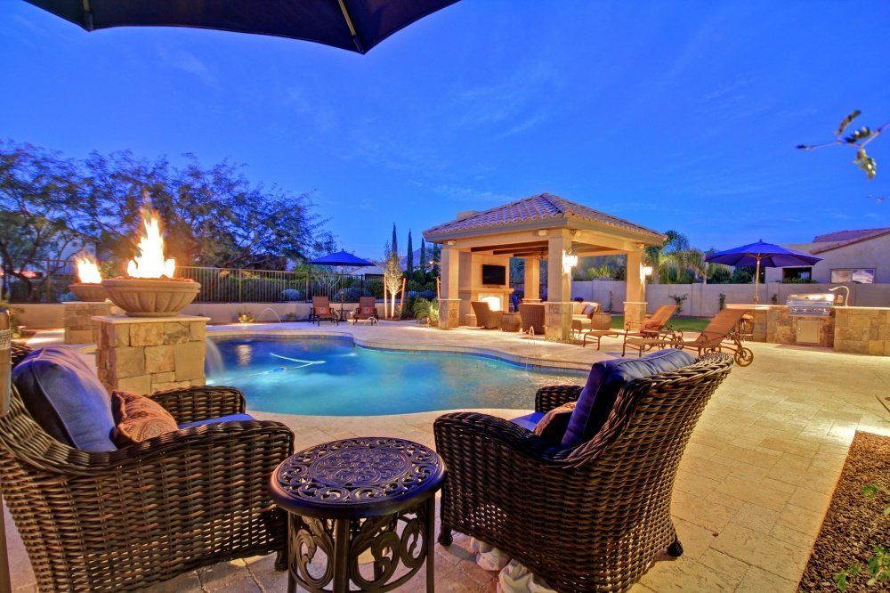 A patio area with chairs , umbrellas and a pool at night.