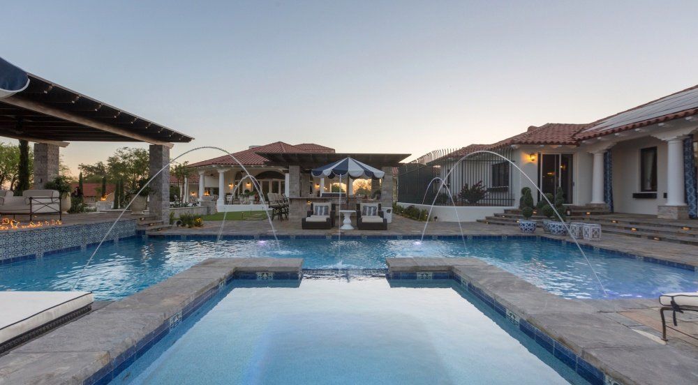 A large swimming pool with a fountain in the middle of it in front of a house.