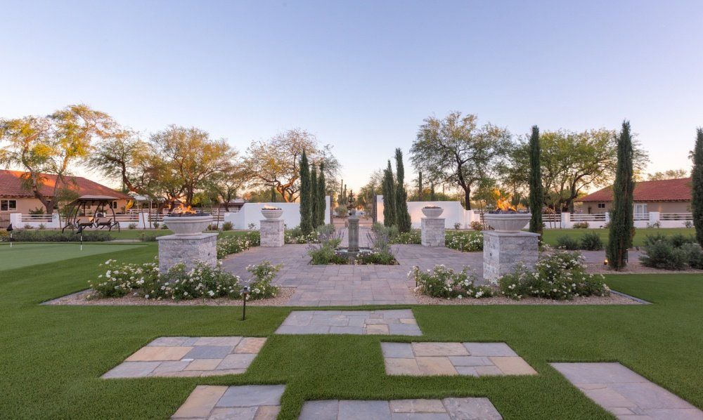 A large lawn with a brick walkway surrounded by trees and flowers.