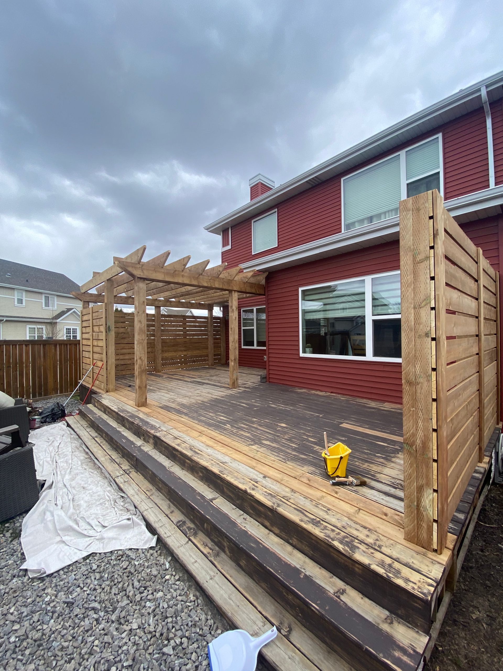 Wooden deck with pergola and privacy screen against a brick house on a cloudy day.