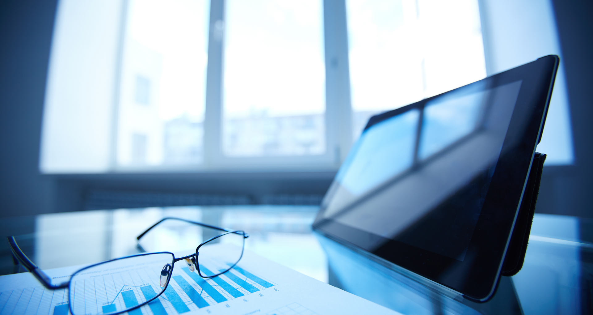 Image of glasses and a tablet sitting on a desk