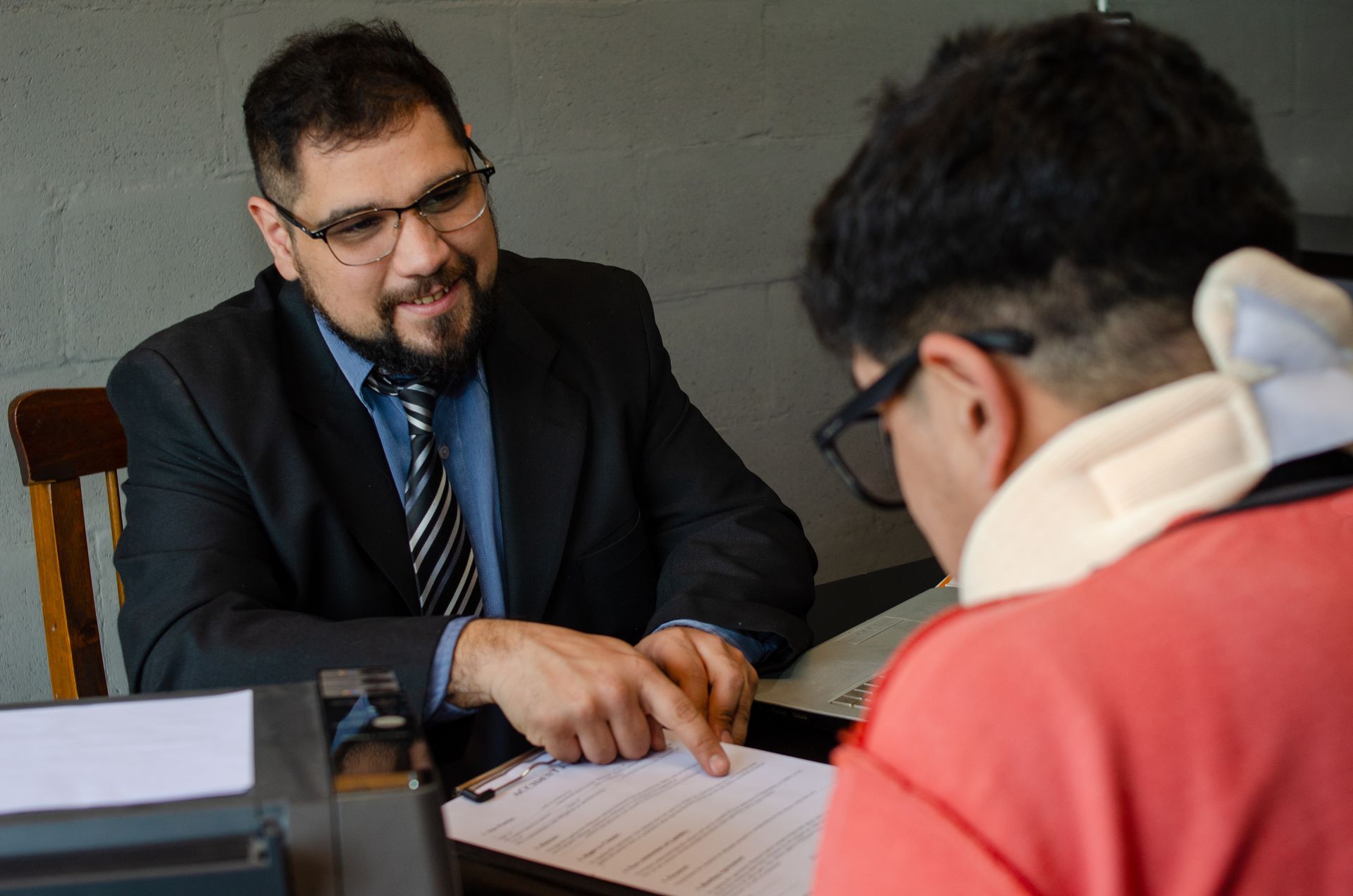 Person in business attire reviewing paperwork with a seated client at a desk. Person in business attire reviewing paperwork with a seated client at a desk.