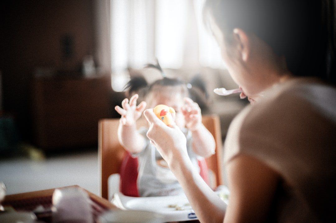 Person feeding a baby at a sunlit table, with the child reaching toward the spoon