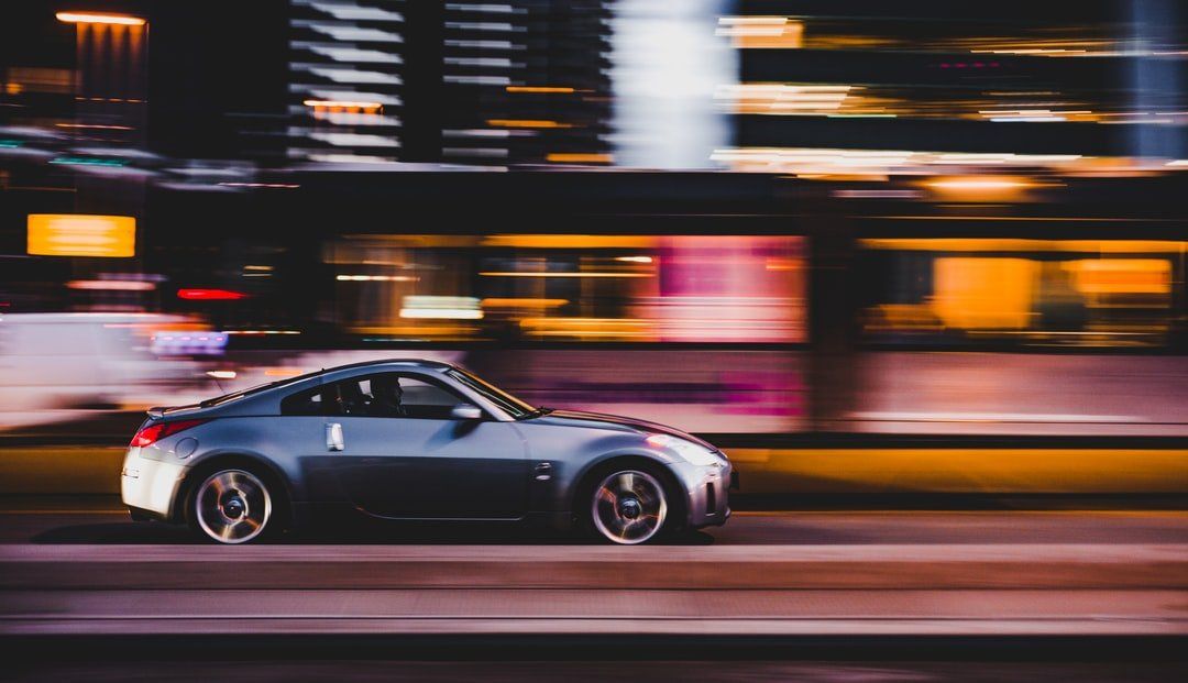 Silver sports car racing fast at night with blurred city lights in the background