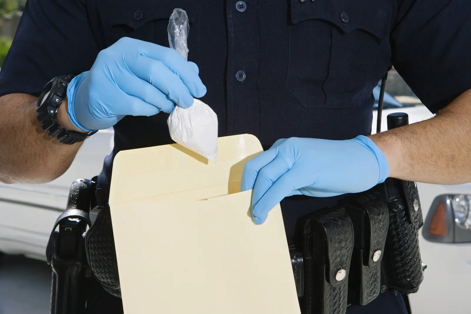Blue-gloved hands handling a clear evidence bag and manila folder on a police officer’s uniformed torso