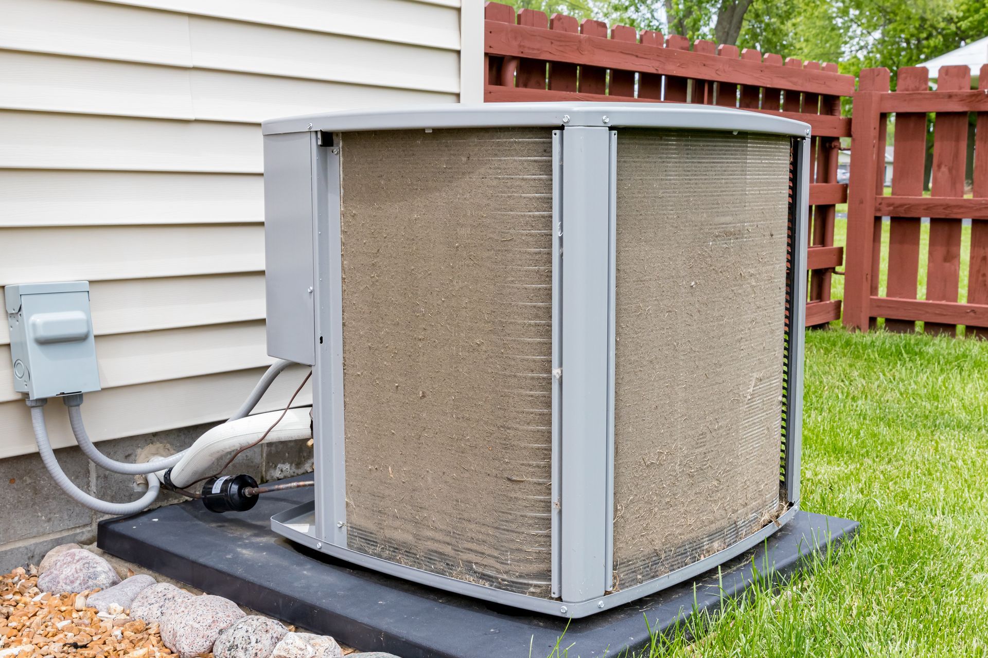 Unité de condensation extérieure d'un climatiseur résidentiel, posée sur une dalle de béton contre une maison au revêtement clair.