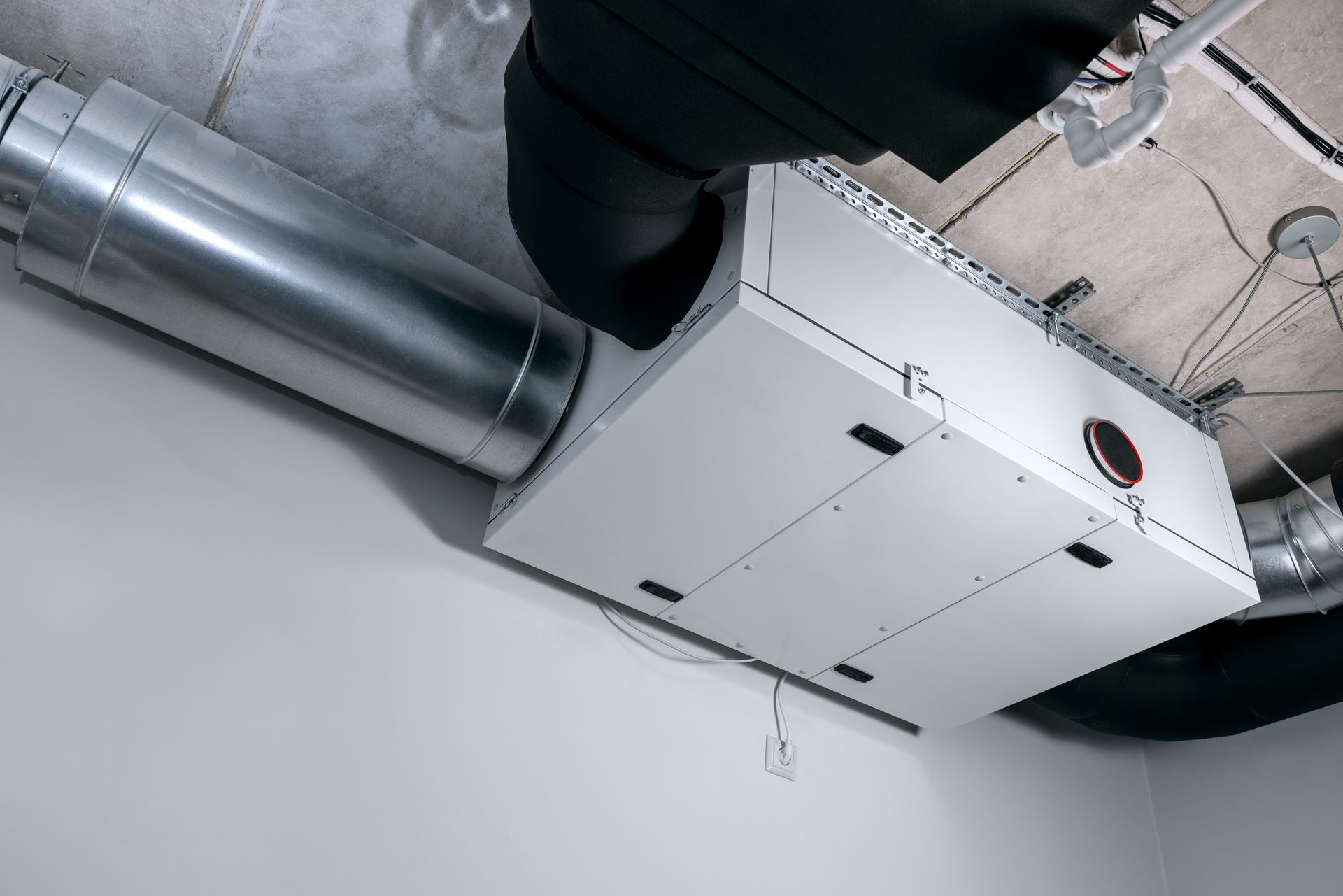 Une unité de traitement d'air CVC blanche, fixée au plafond, avec des conduits métalliques et isolés noirs raccordés, dans un espace intérieur.