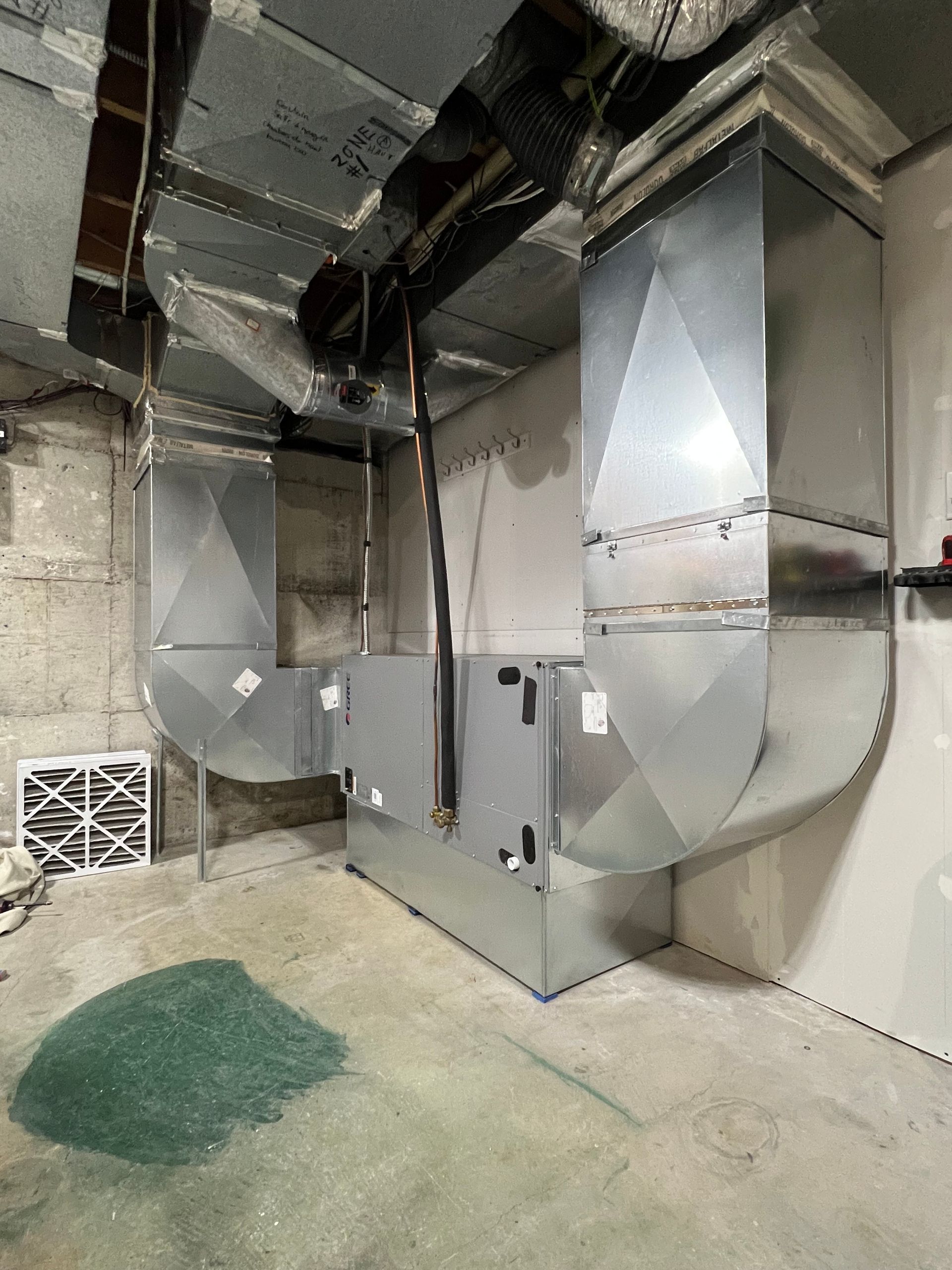 Une unité de chauffage, ventilation et climatisation en métal, avec des conduits rectangulaires intégrés, est posée sur un sol en béton dans un sous-sol.