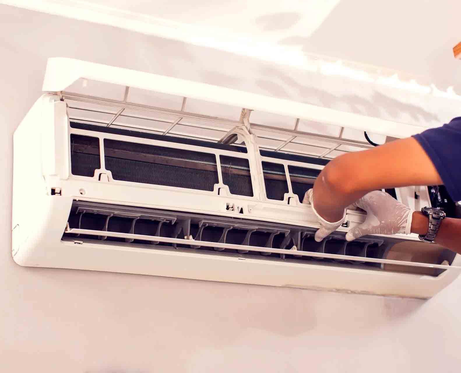 Un technicien portant des gants blancs effectue la maintenance du panneau interne ouvert d'un climatiseur mural blanc.