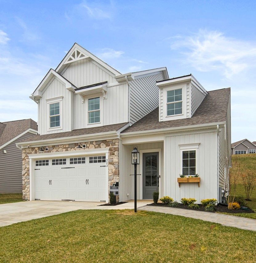White house with stone accents, garage, and a lamppost on a green lawn under a blue sky.