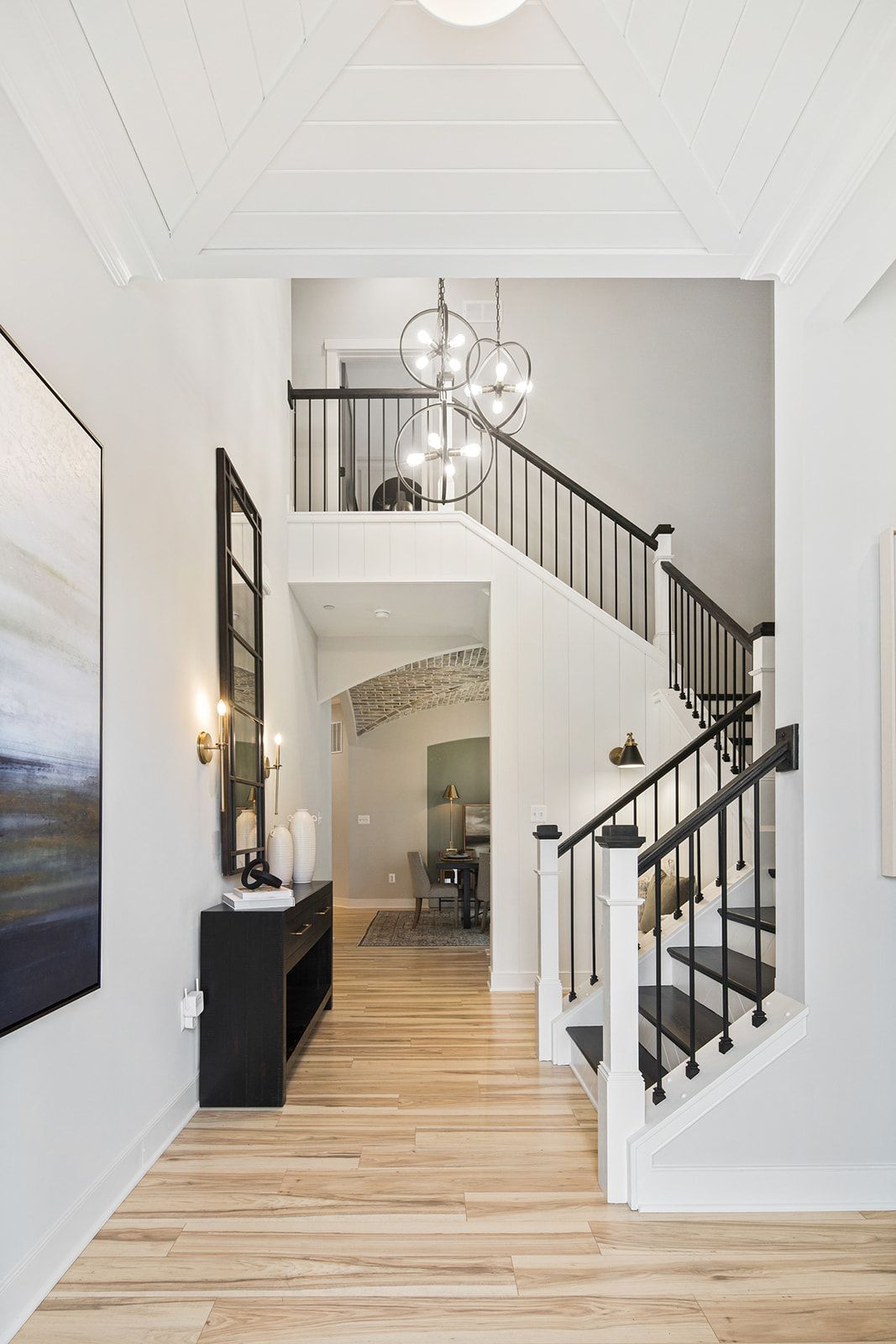 Entryway with stairs, black and white accents, light wood floors, abstract art, chandelier, and a console table.