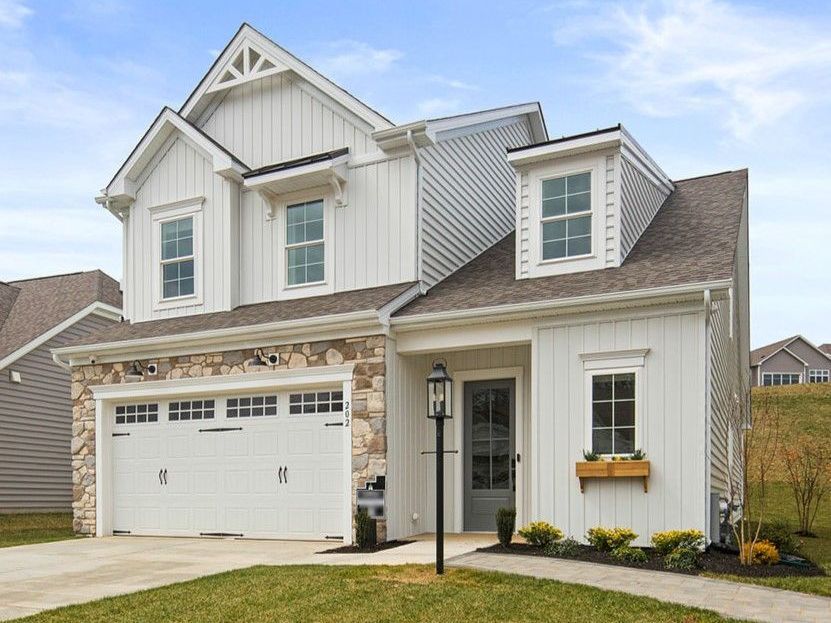 Two-story white house with stone accents and attached garage on a grassy lot.