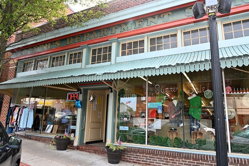 A vintage clothing store with a teal awning, clothes in window displays, and a brick building.