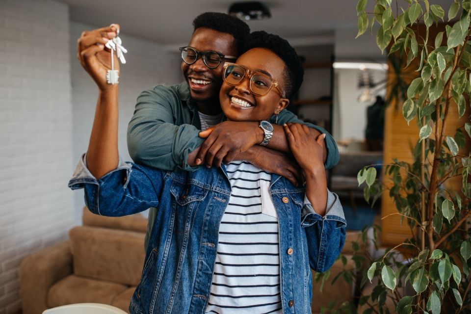 Couple embracing, smiling, holding keys in new home.
