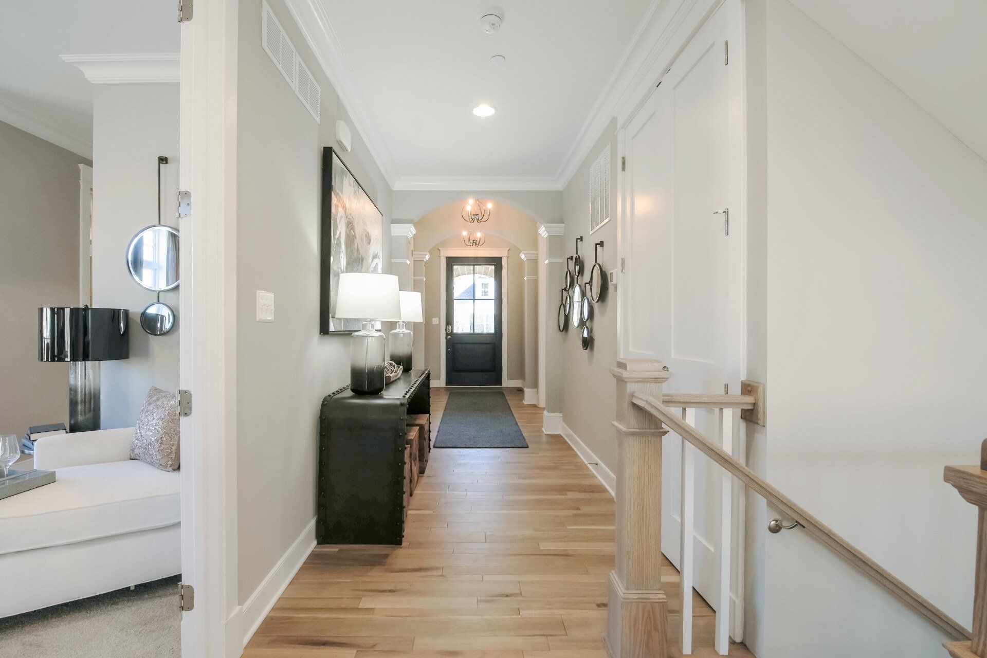Hallway with hardwood floors, gray walls, and white trim, leading to a black door with a rug.
