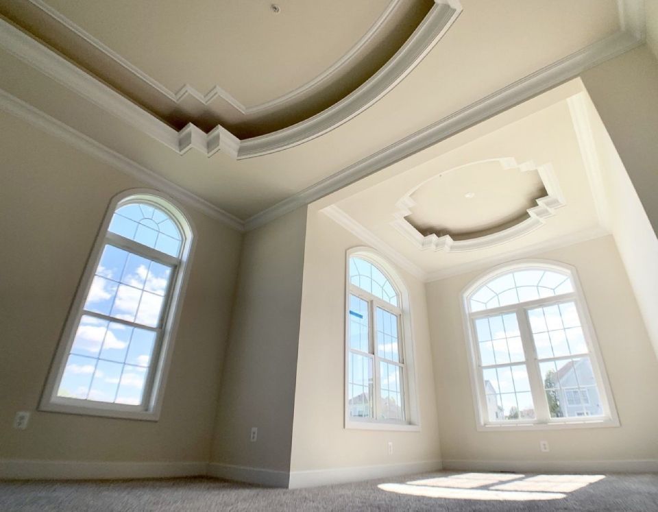 Empty room with arched windows, ornate ceiling trim, and beige walls.