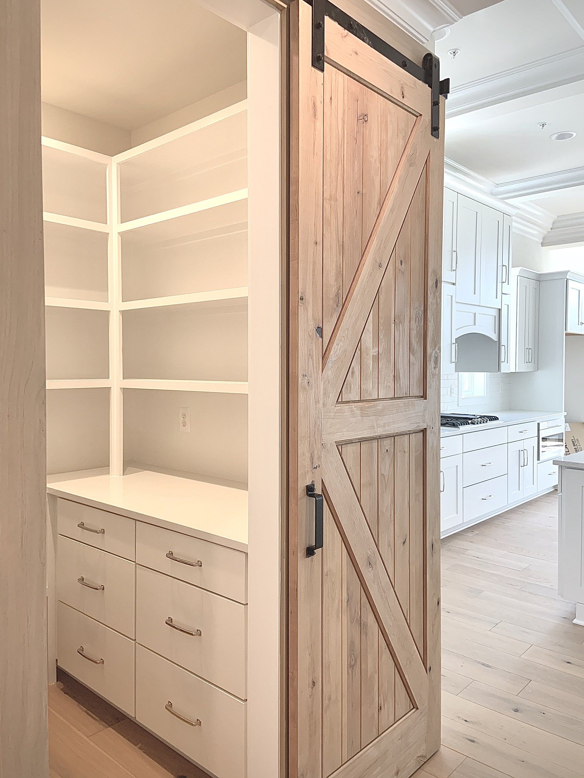 Barn door pantry entrance with white shelving and cabinets in a kitchen.