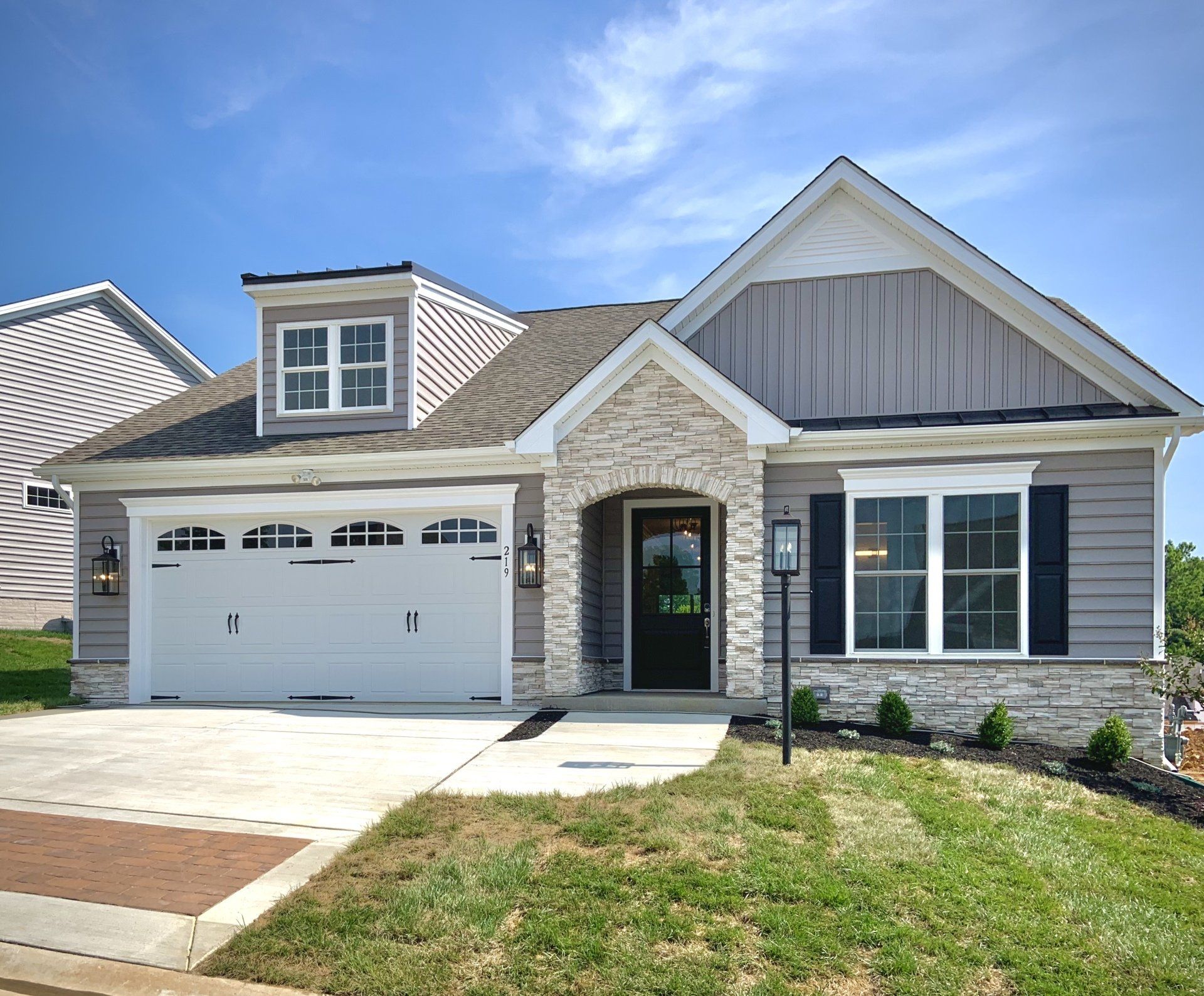 Ranch-style house with gray siding, white trim, and stone accents under a blue sky.