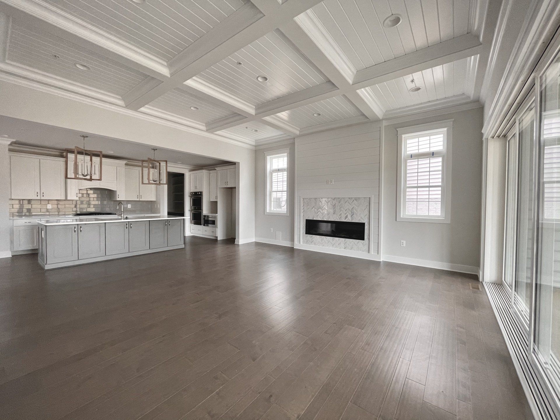 Empty, light-filled living space with wood floors, kitchen, fireplace, and windows.