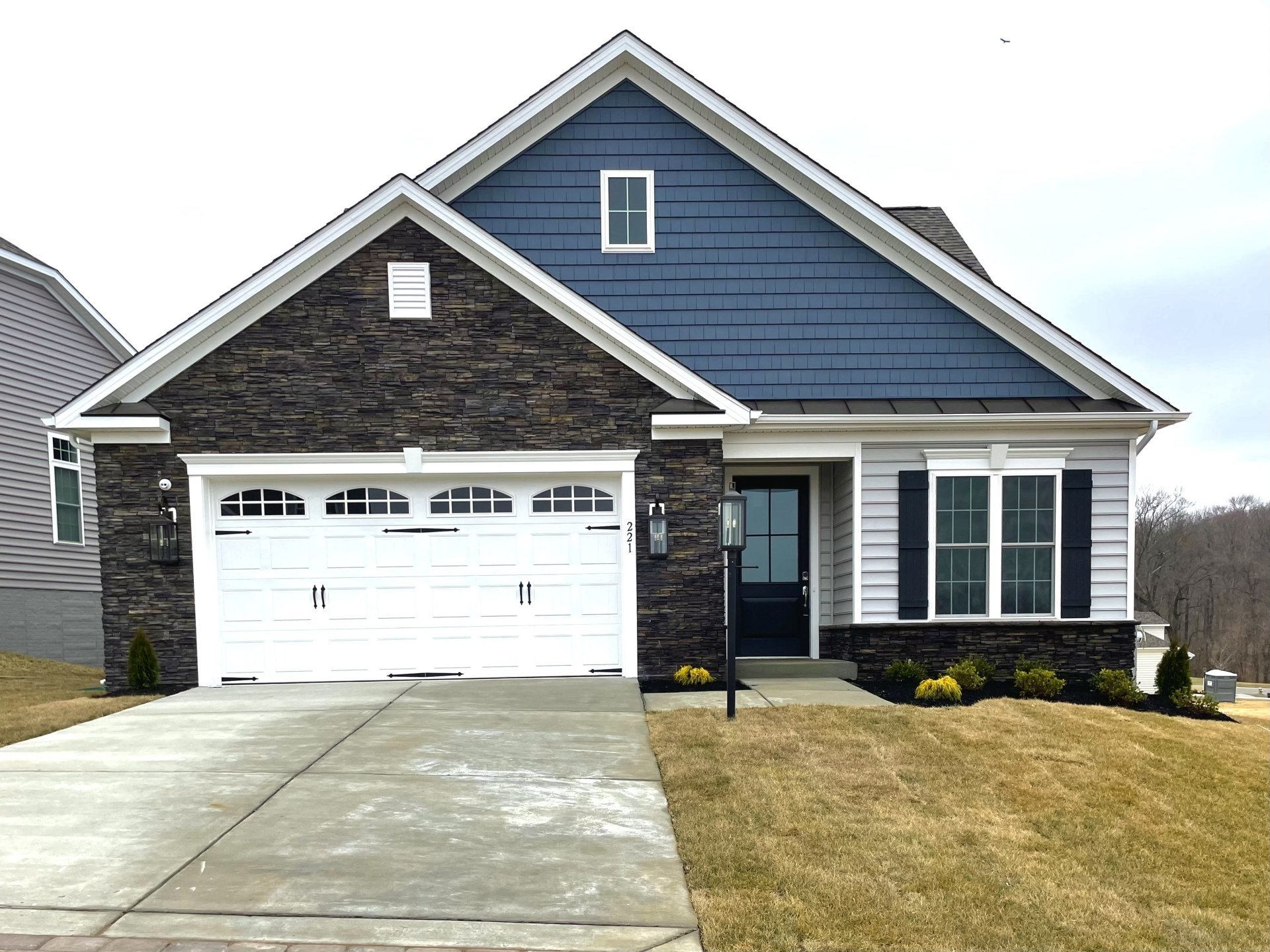 Single-story house with stone and blue siding, white garage door, black shutters, and a paved driveway.
