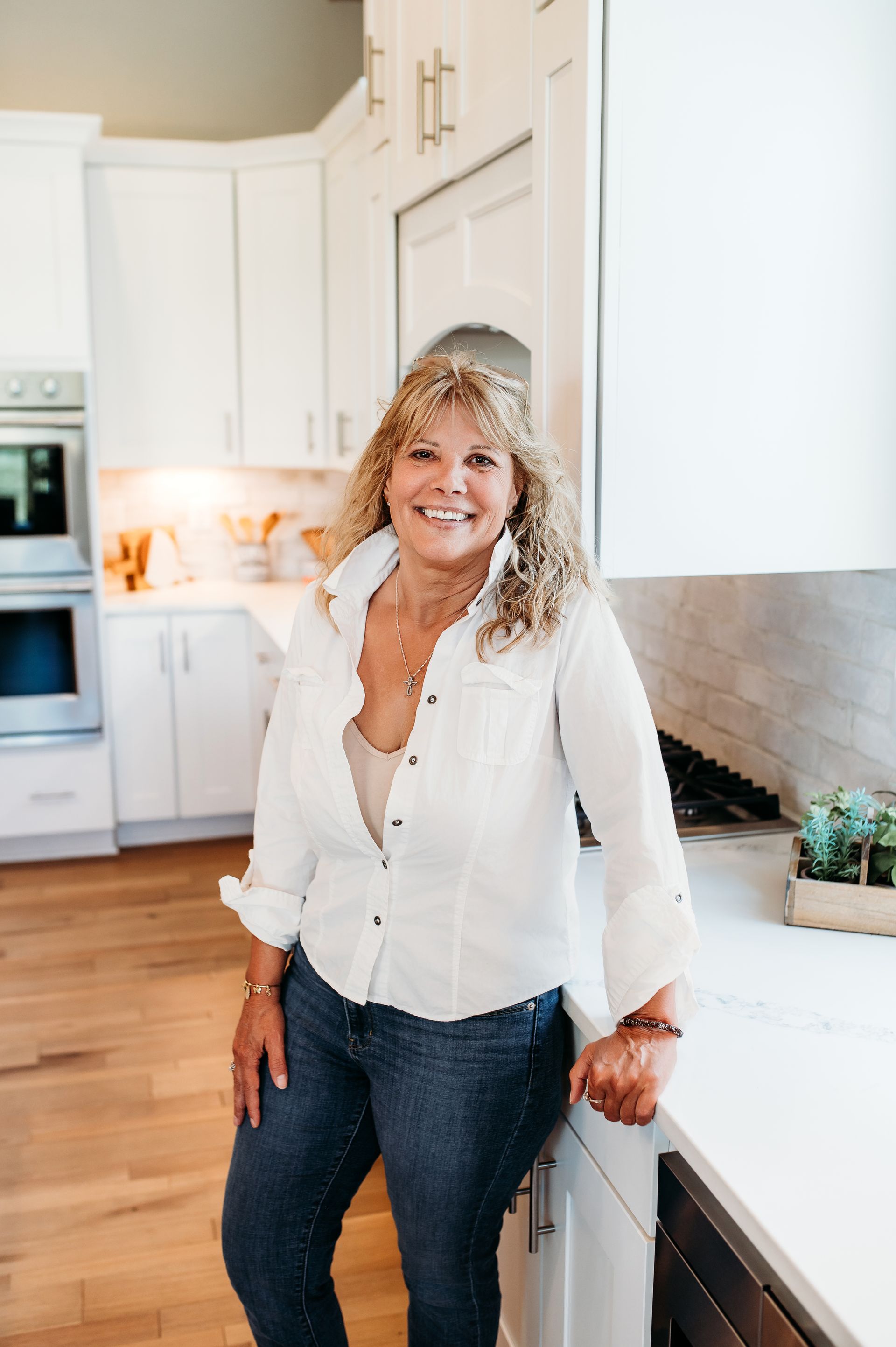 Woman in white shirt and jeans smiles in a bright kitchen.