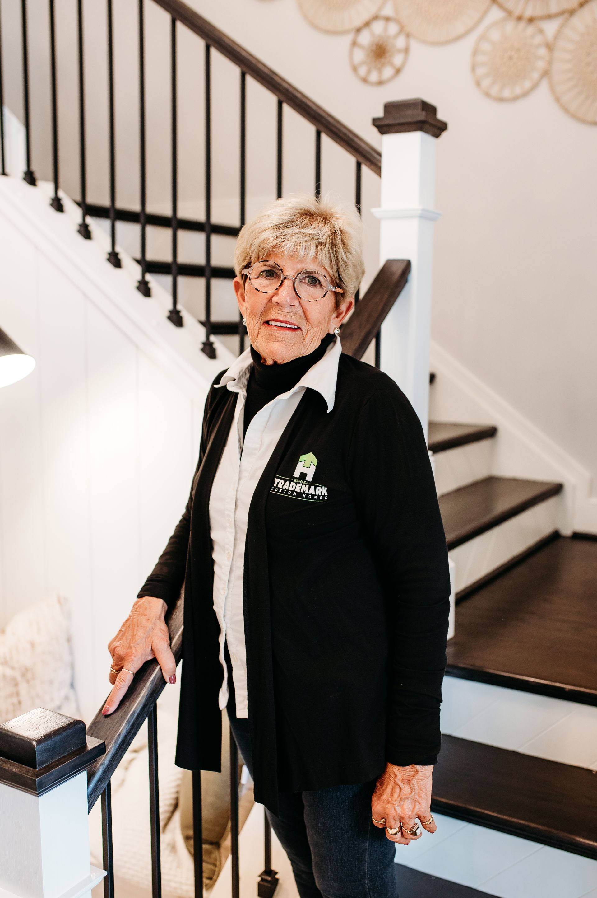 Elderly woman in black sweater, standing on a staircase with a handrail.