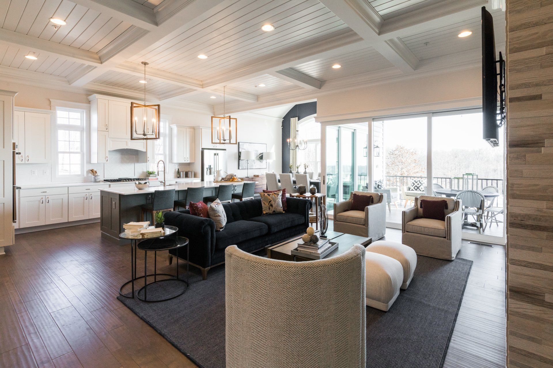 Open-concept living space with kitchen, seating area, and outdoor patio access. Dark blue sofa, cream armchairs, and dark wood flooring.