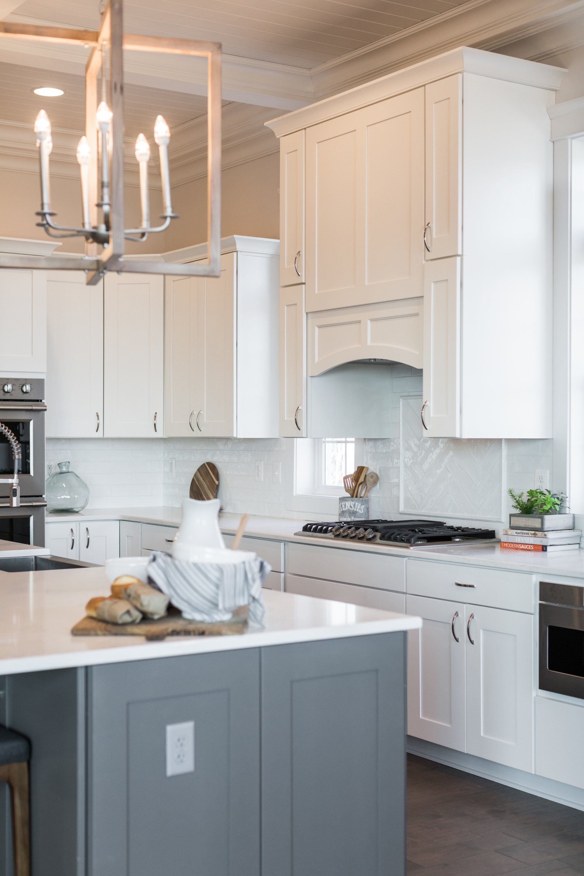 Modern white kitchen with gray island and chandelier.