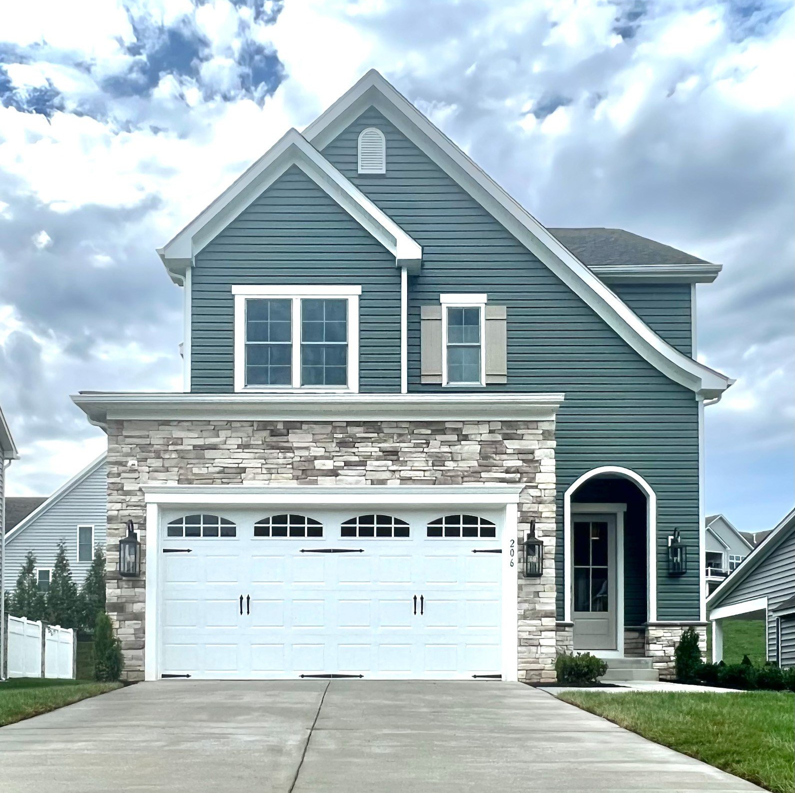 Two-story house with stone and blue siding, white garage door, and driveway against a cloudy sky.