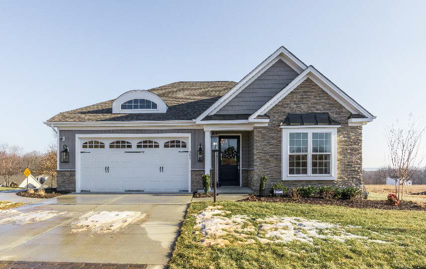 Gray and stone-fronted single-story house with a driveway, front yard, and blue sky background.