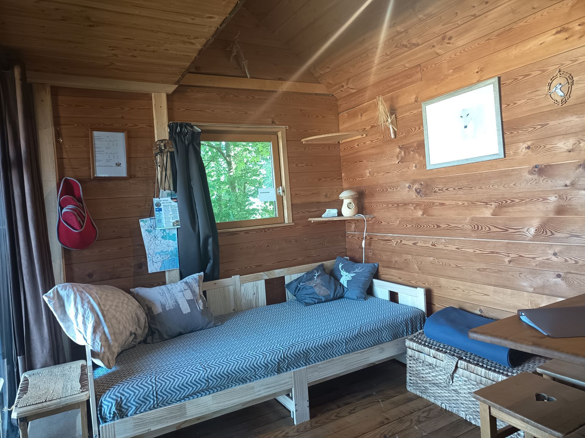 Gezellig interieur van een boomhut met een bank, een glazen schuifdeur naar een balkon en een klein raam met een gordijn.