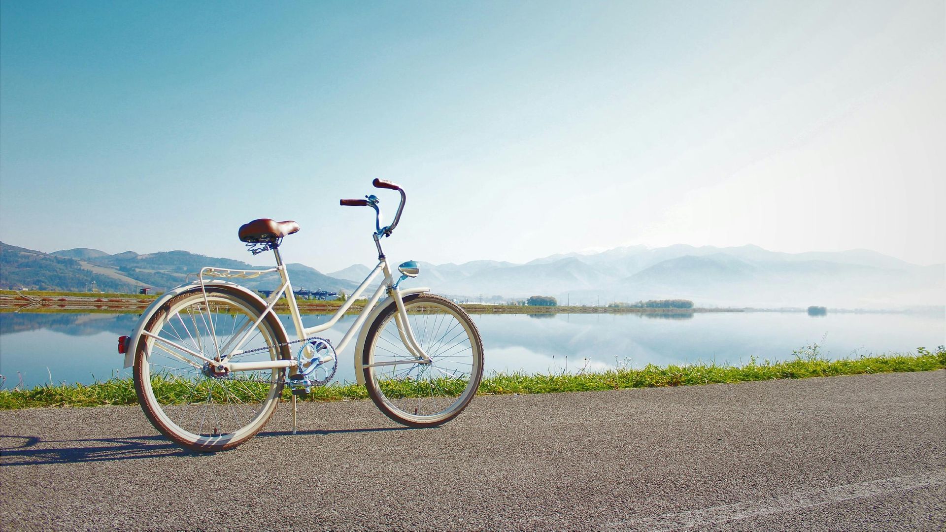 Een witte fiets staat geparkeerd op een pad met uitzicht op een meer en bergen onder een helderblauwe hemel.