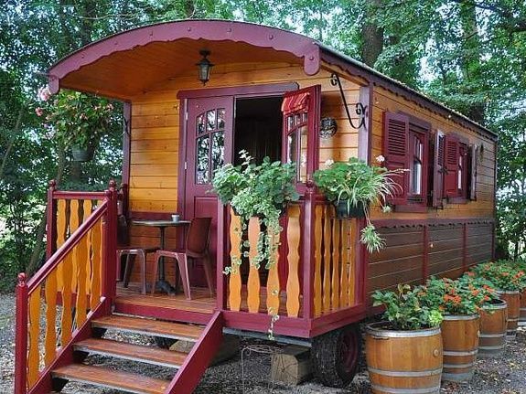 Houten zigeunerwagen met veranda en potplanten.