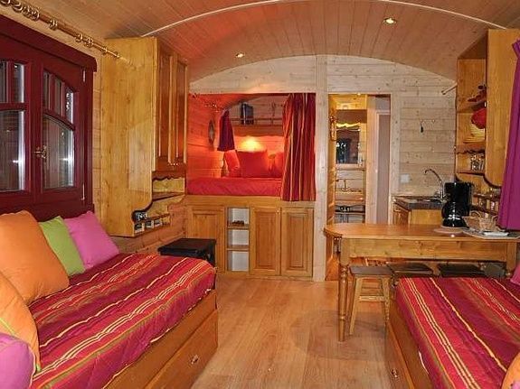 Gezellig interieur van een woonwagen. Rood en oranje beddengoed, houten meubels, rode raamkozijnen.