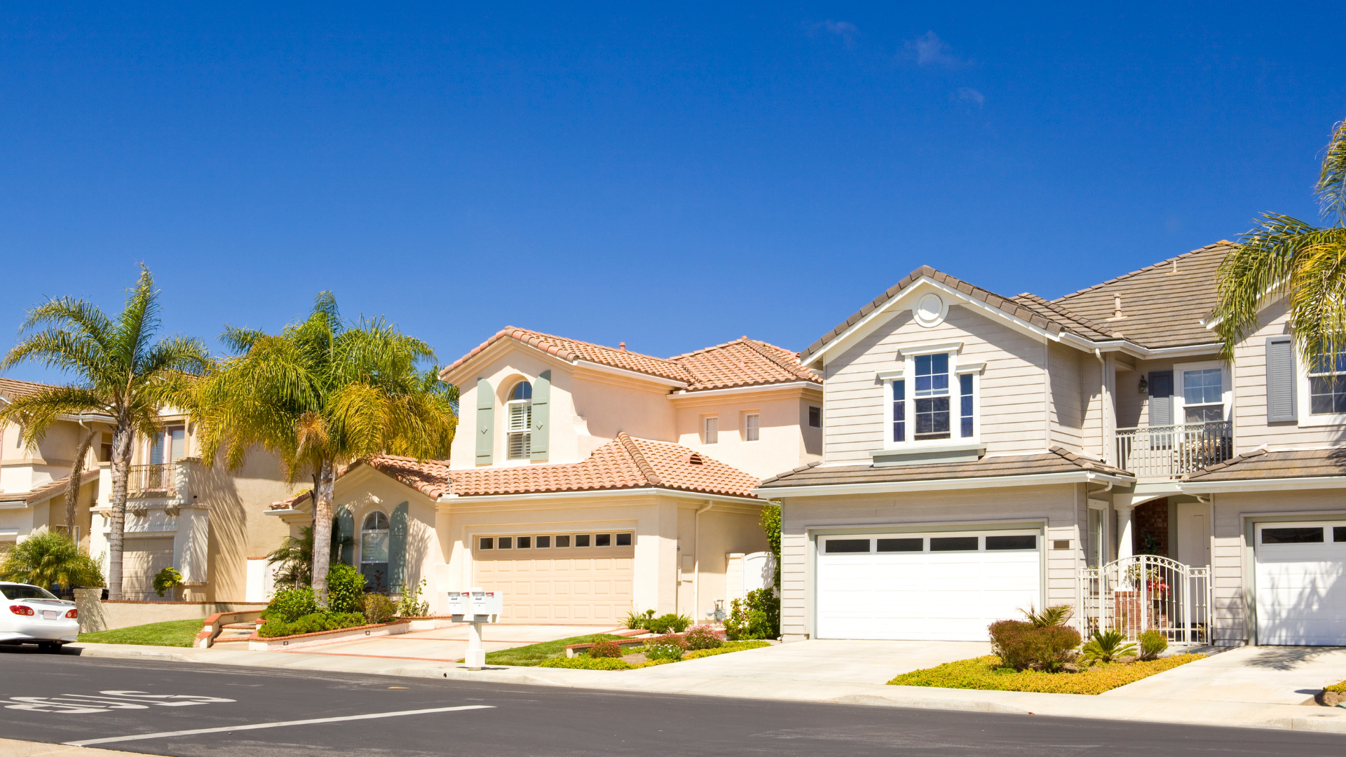 Stone houses with arched entryways and landscaped flower beds along a quiet residential street