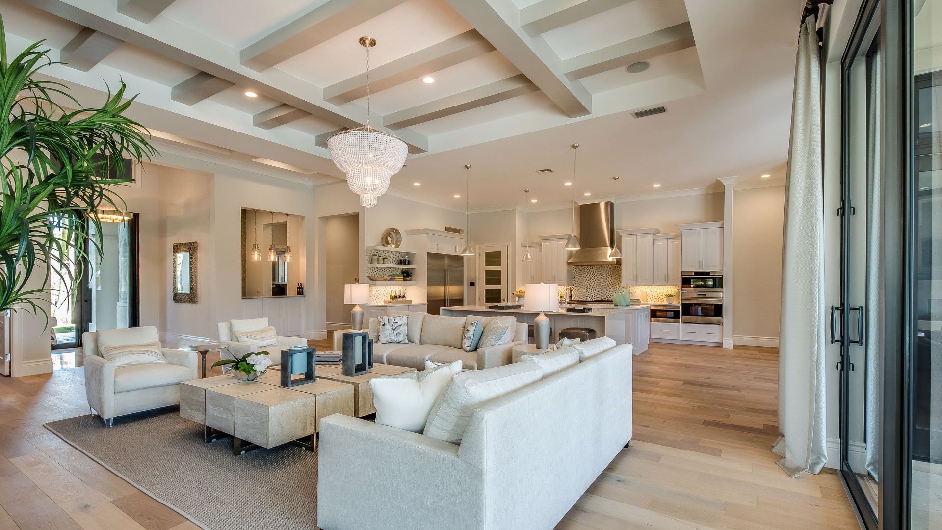 Spacious modern living room with white sofas, chandelier, and open kitchen in a bright neutral interior