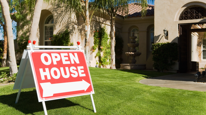 Hand holding house keys in front of a modern home for sale
